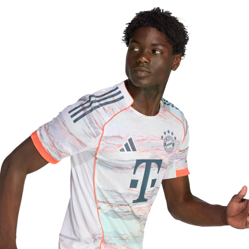 A young Black man with curly hair wearing a white patterned FC Bayern Munich soccer jersey, looking to his left in a dynamic running pose.