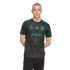 A young man with short blonde hair wearing a black and green Tigres UANL soccer jersey and black jeans, standing against a black background.