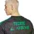 Side profile of a blonde man wearing a grey patterned jersey with green "TECATE" and "AFIRME" text on the back. Solid black background.