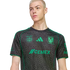 A person with short blonde hair wearing a grey and green patterned Tigres UANL soccer jersey against a black background.