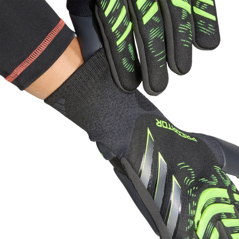 Close-up of black and neon green goalkeeper gloves being put on, highlighting the textured fingers and ribbed wrist cuff against a black background.