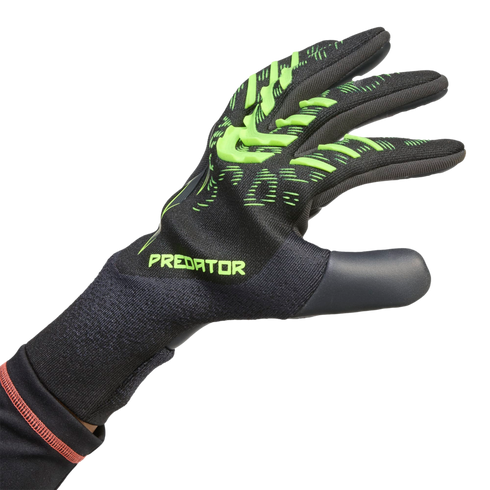Hand wearing a black Adidas Predator goalkeeper glove with neon green textured zones and "PREDATOR" branding on the back, against a black background.