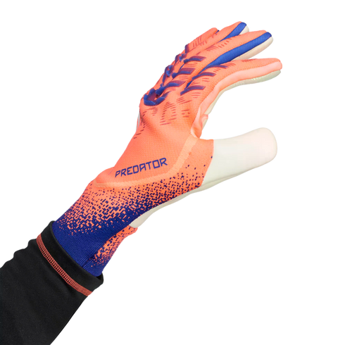 An orange and blue Adidas Predator goalkeeper glove worn on a hand, reaching out against a black background.