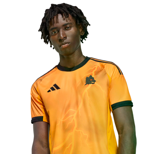 A man with dreadlocks wearing an orange Adidas jersey with a wolf crest and lightning bolt graphics against a black background.