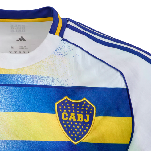 Close-up of a white, blue, and yellow Boca Juniors jersey featuring the CABJ crest on a blue band, three blue stripes on the shoulder, and internal Adidas branding.