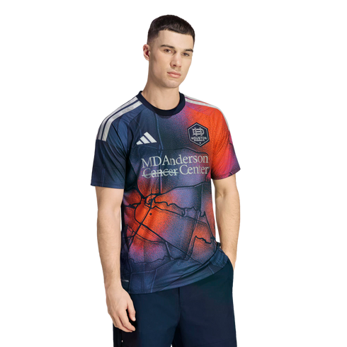 A man models a navy Houston Dynamo FC soccer jersey featuring a red and orange map pattern and the MD Anderson Cancer Center logo.