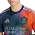 A person wears a Houston Dynamo FC soccer jersey with a pixelated blue-to-orange gradient, featuring the team crest, Adidas logo, and MD Anderson Cancer Center sponsorship.