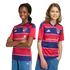 Two smiling young fans wearing red and blue striped FC Dallas home jerseys and blue shorts, posing against a black background.