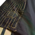 Close-up of a black sports jersey with gold geometric line patterns and a small badge of a football pitch. The fabric has a fine mesh texture.