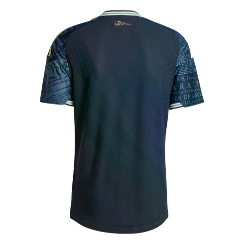 Back of a navy soccer jersey with US Constitution script on the sleeves, a gold snake logo below the collar, and light blue trim on the neck and cuffs.