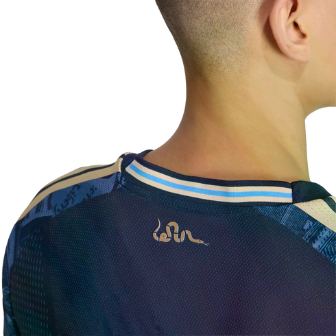 A close-up back view of a person's head and neck wearing a navy blue jersey with a small rattlesnake logo and a light blue and tan striped collar.