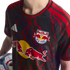 A person wears a black New York Red Bulls soccer jersey with red lightning patterns and prominent team logos, while holding an MLS soccer ball.