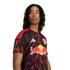 A person with long dreadlocks wearing a black and red lightning-patterned New York Red Bulls soccer jersey against a black background.
