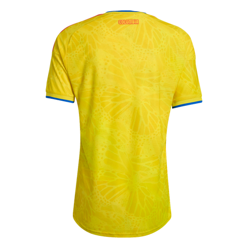 Back view of a yellow Colombia soccer jersey with a tone-on-tone butterfly pattern, red "COLOMBIA" text at the neck, and blue-and-red trim on the collar and sleeves.
