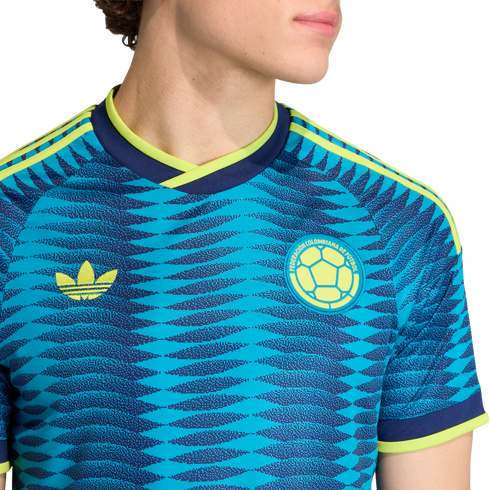 Blue Colombia soccer jersey with a zigzag pattern, yellow Adidas Trefoil logo, and team crest. Features neon yellow accents on the collar and sleeves.