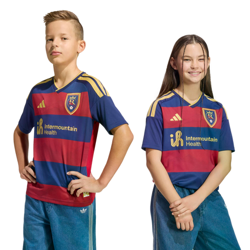Two children, a boy and a girl, pose in matching navy and red striped soccer jerseys with gold logos against a black background.
