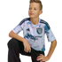 A young boy with brown hair kneeling, wearing a tie-dye San Jose Earthquakes soccer jersey and black pants against a black background.