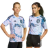 Two kids pose in matching light blue and pink tie-dye San Jose Earthquakes soccer jerseys and black shorts against a solid black background.