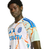 A portrait of a man wearing a white San Diego FC soccer jersey with blue and orange abstract patterns against a black background.