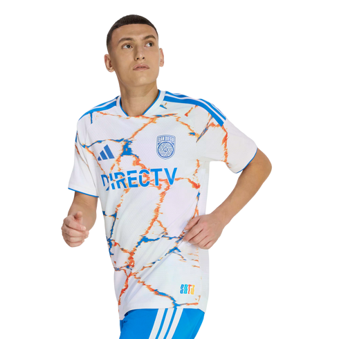 A man wearing a white San Diego FC soccer jersey with blue and orange marble patterns and DirecTV logo, in a running pose against a black background.