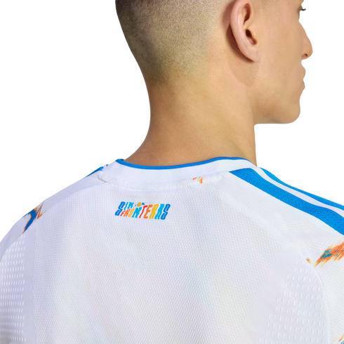 A close-up of the back of a man's neck and upper back, wearing a white jersey with blue trim and a colorful "SIN FRONTERAS" graphic on the neck.