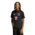 A smiling person with dreadlocks wearing a black Inter Miami CF soccer polo shirt with pink logos, set against a solid black background.