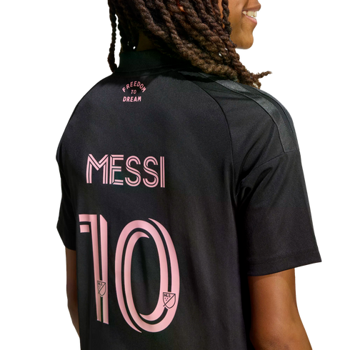 Back view of a person with long braids wearing a black Inter Miami jersey with pink lettering for "FREEDOM TO DREAM", "MESSI", and the number 10 on a black background.