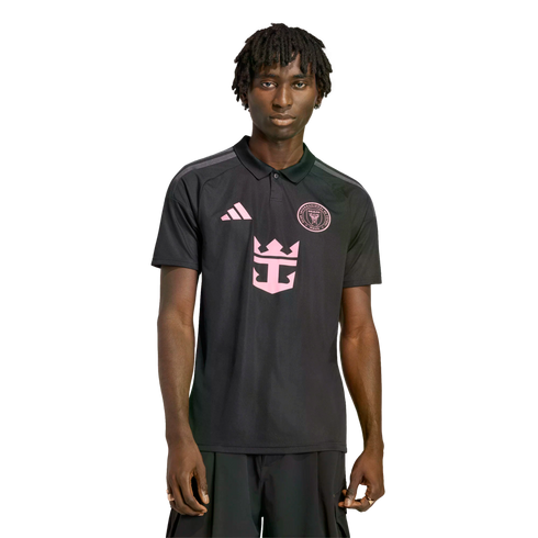 A man with dreadlocks wearing a black Inter Miami CF polo shirt with pink Adidas, team crest, and Royal Caribbean logos, isolated against a black background.