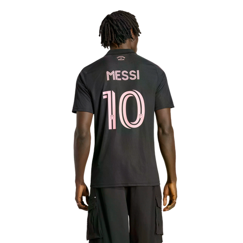 Back view of a man with dreadlocks wearing a black Inter Miami CF soccer jersey with "MESSI" and number "10" in pink. He is standing against a solid black background.