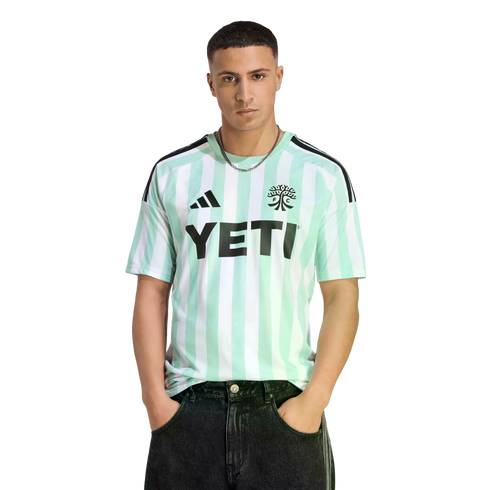 Man wearing a mint green and white striped soccer jersey with a black "YETI" logo on the chest, paired with black jeans against a black background.