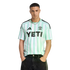 Man wearing a mint green and white striped soccer jersey with a black "YETI" logo on the chest, paired with black jeans against a black background.