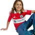 A smiling child with long wavy hair wears a red and white Chicago Fire FC soccer jersey and blue jeans, sitting against a black background.