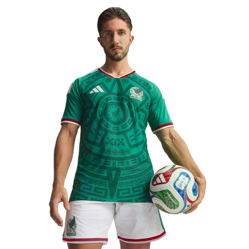 A male soccer player poses in a green Mexico national team jersey and white shorts, holding a soccer ball against a black background.