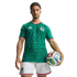 A male soccer player poses in a green Mexico national team jersey and white shorts, holding a soccer ball against a black background.
