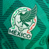 Close-up of the Mexico national football team crest on a green textured jersey. The emblem features a stylized eagle, a soccer ball, and the word "MÉXICO".
