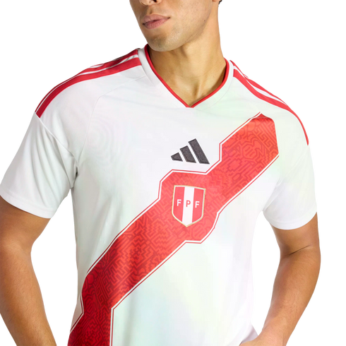 A person wearing the white Peru national soccer team home jersey, featuring a prominent red diagonal sash with geometric patterns and the team's crest.
