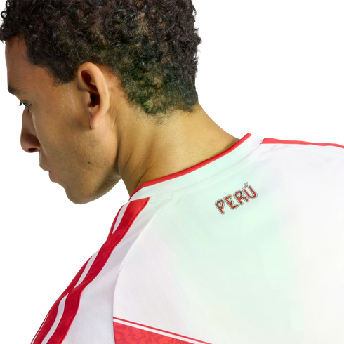 Profile view of a man wearing a white Peru national team jersey with red stripes and the word "PERÚ" on the back collar against a black background.