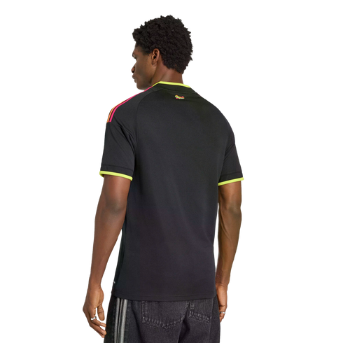 Rear view of a man wearing a black shirt with neon yellow trim and multi-colored shoulder stripes against a black background.