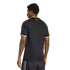 Rear view of a man wearing a black shirt with neon yellow trim and multi-colored shoulder stripes against a black background.