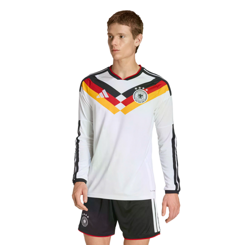 A man modeling a white long-sleeved Germany soccer jersey with a black, red, and yellow chevron design and matching black shorts against a solid black background.