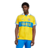 A young man with dark skin wears a yellow and blue Tigres UANL soccer jersey and blue pants against a solid black background.