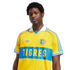 A man wearing a yellow and blue Adidas Tigres UANL soccer jersey with a white collar against a black background.
