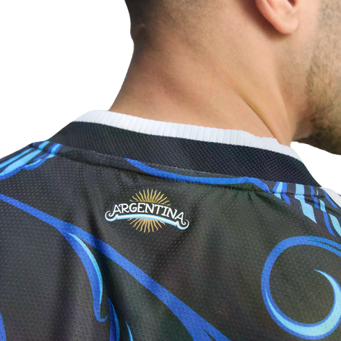 Close-up of a person wearing a black jersey with blue swirls. A small logo on the back reads "ARGENTINA" beneath a golden sun. The background is solid black.