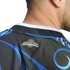 Close-up of a person wearing a black jersey with blue swirls. A small logo on the back reads "ARGENTINA" beneath a golden sun. The background is solid black.