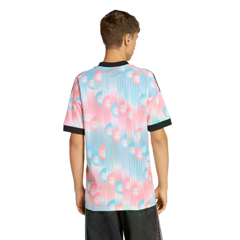 A man from behind in a t-shirt with a pink and blue spherical pattern and black trim, paired with dark jeans, set against a black background.