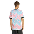 A man from behind in a t-shirt with a pink and blue spherical pattern and black trim, paired with dark jeans, set against a black background.