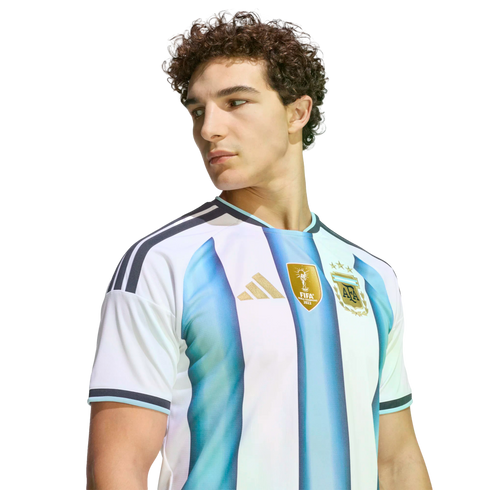 A young man with curly hair wearing an Argentina national team soccer jersey, looking to the side against a solid black background.
