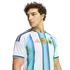 A young man with curly hair wearing an Argentina national team soccer jersey, looking to the side against a solid black background.