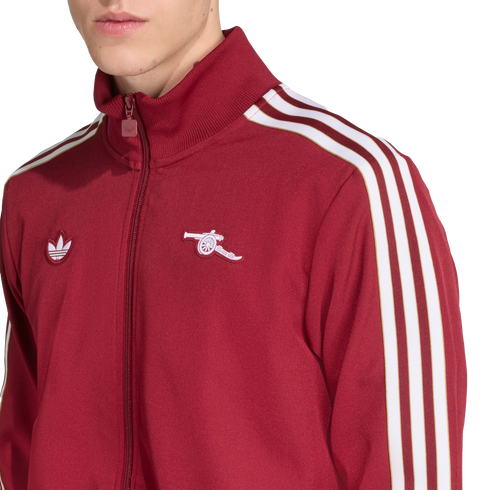 A person wears a maroon Adidas track jacket featuring three white stripes on the sleeves and the Arsenal FC cannon logo on the left chest.
