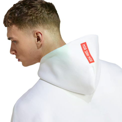 Side profile of a man wearing a white hoodie. The hood features a red rectangular patch with the white text "MIA SAN MIA".